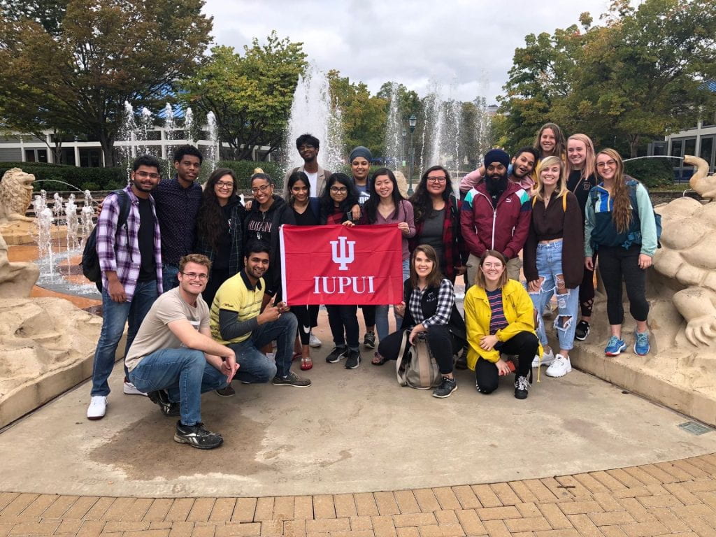 Photo of Medha with group of students and an IUPUI flag